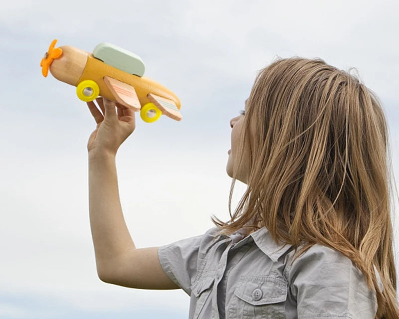 Child holding a wooden toy airplane outdoors against a blue sky